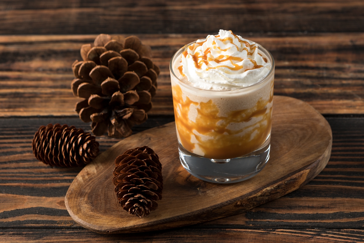 caramel cocktail with whipped cream on top and pine cones beside it