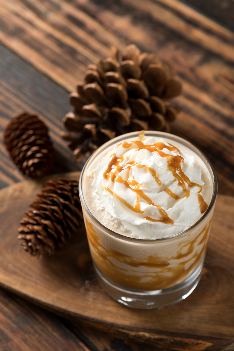 caramel cocktail with whipped cream on top and pine cones beside it